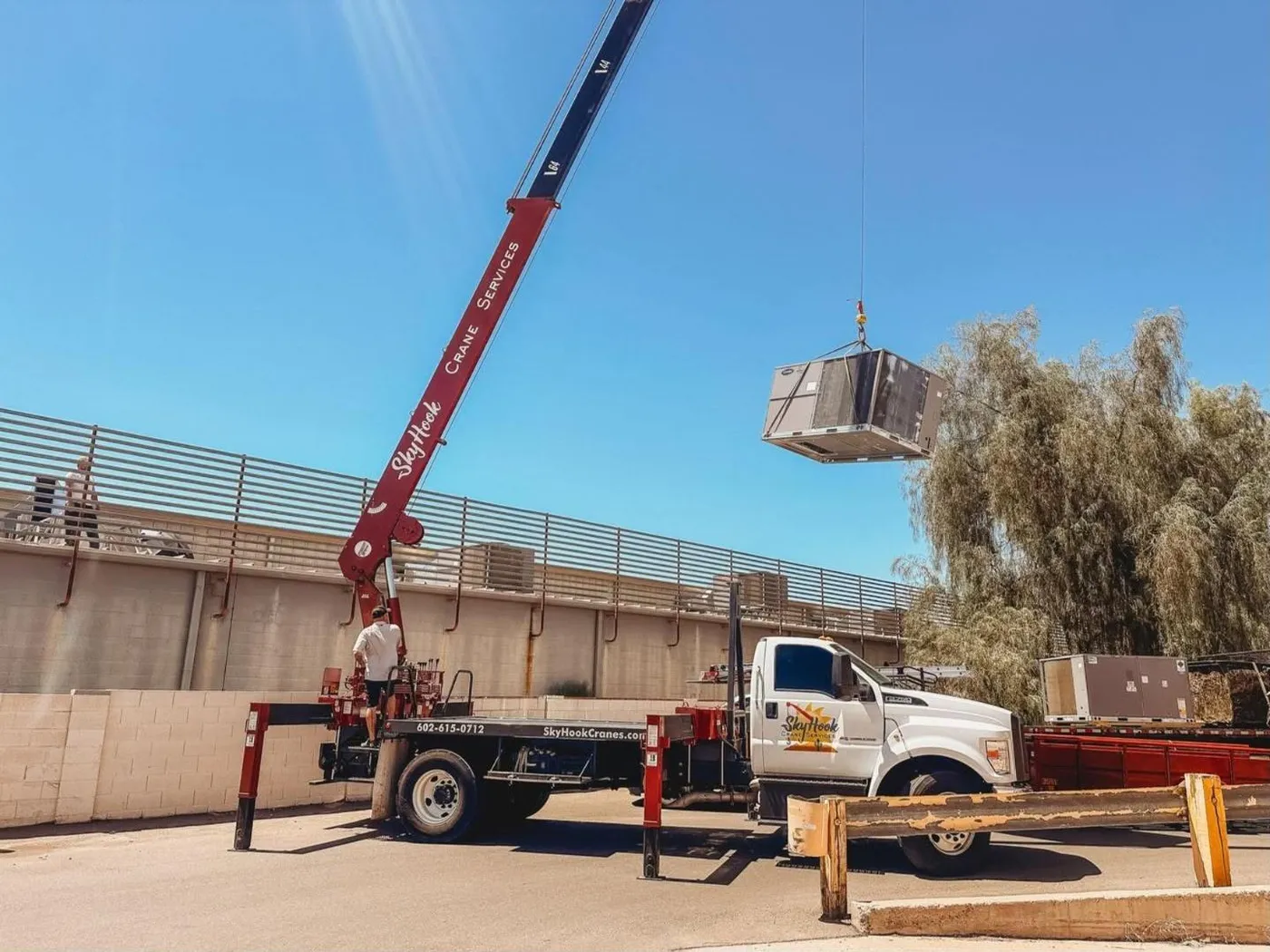 Skyhook crane swinging a commercial rooftop HVAC unit over a parapet