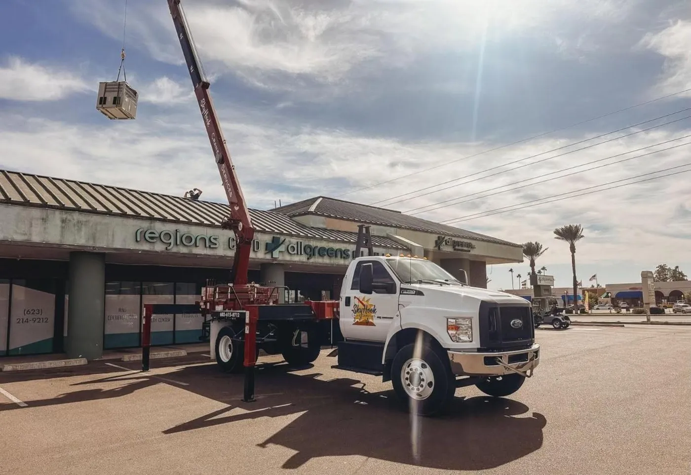 Crane lifting a commercial rooftop HVAC unit onto a strip-center roof