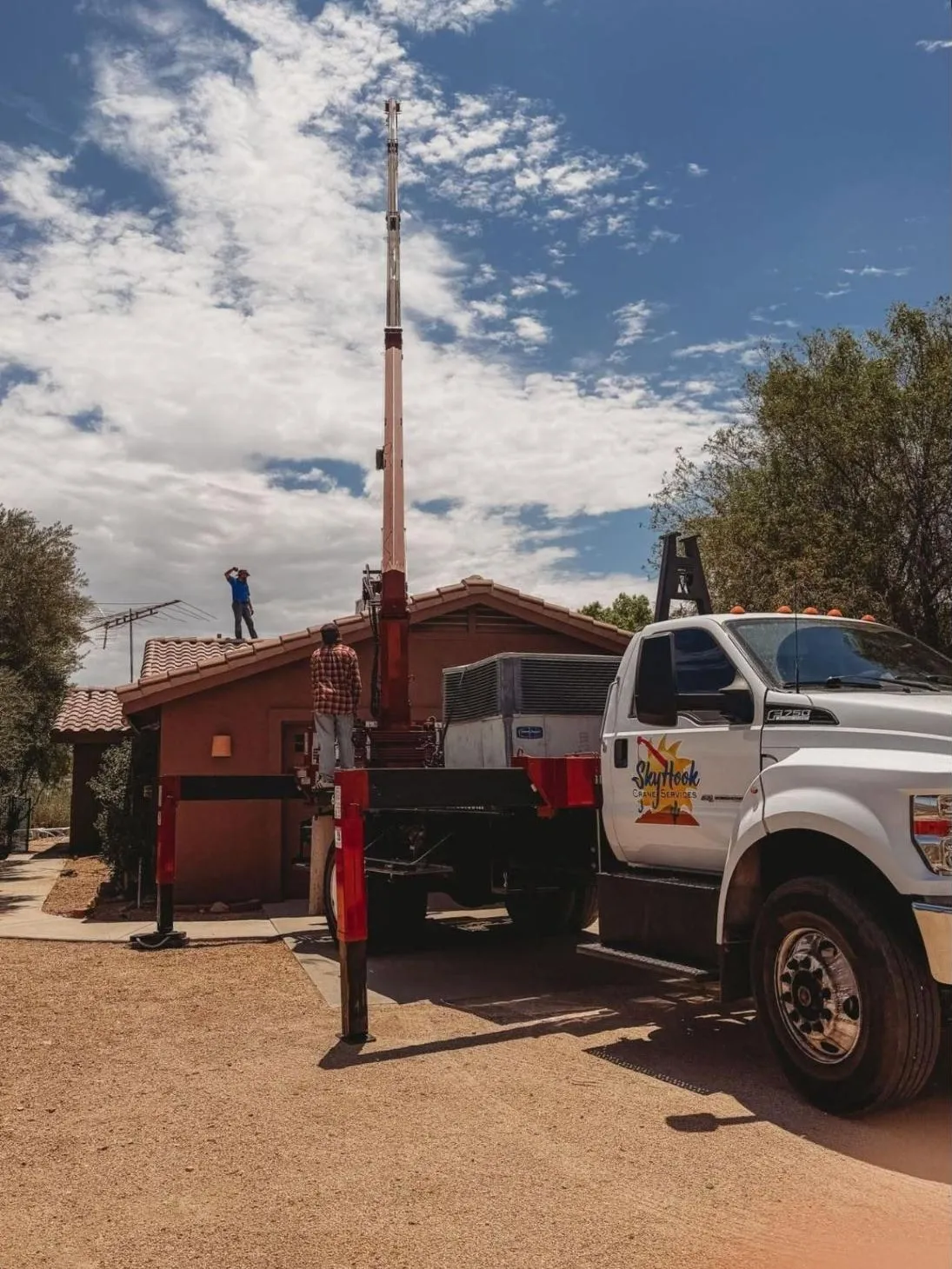 Skyhook crane setting a rooftop HVAC unit on a tile-roof home